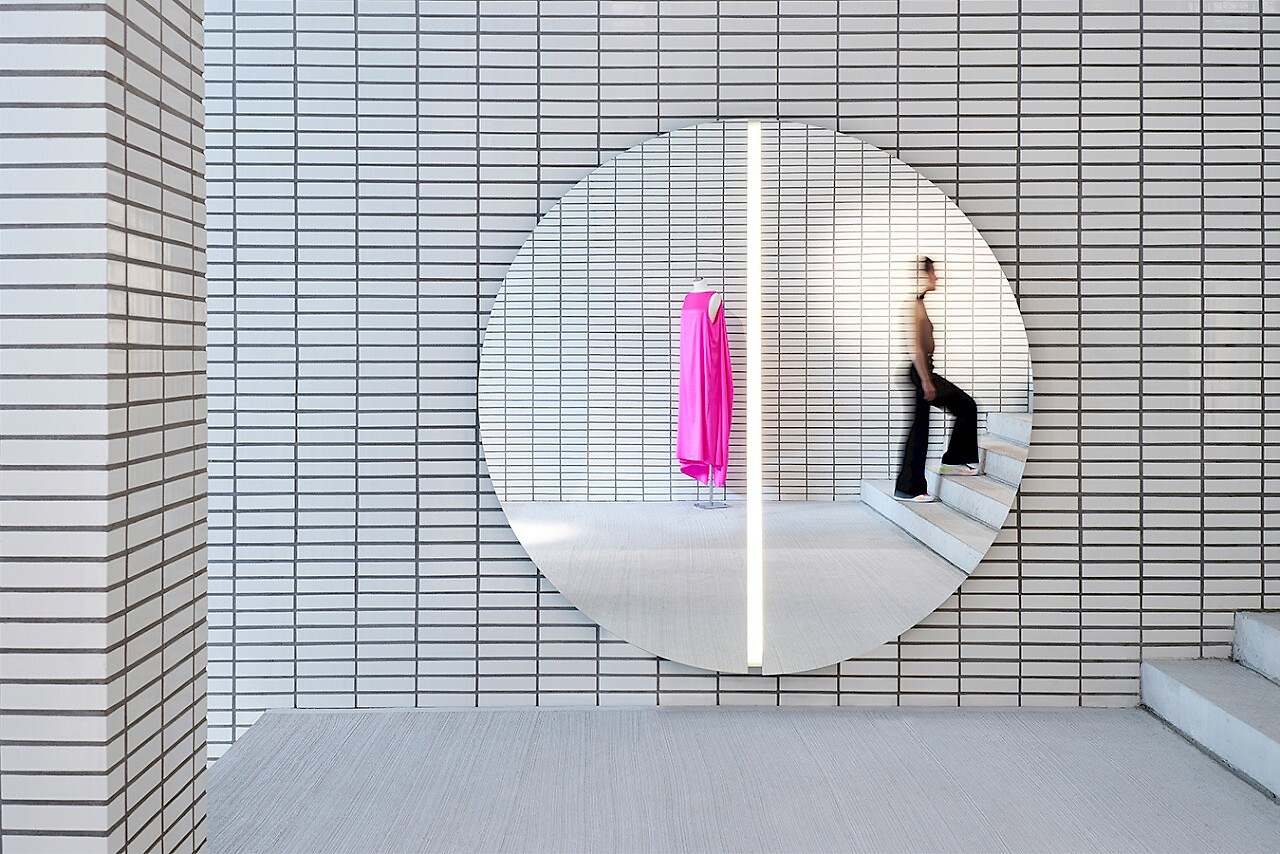 Runder Wandspiegel mit vertikalem Lichtband in modernem Raum mit weißer Fliesenstruktur