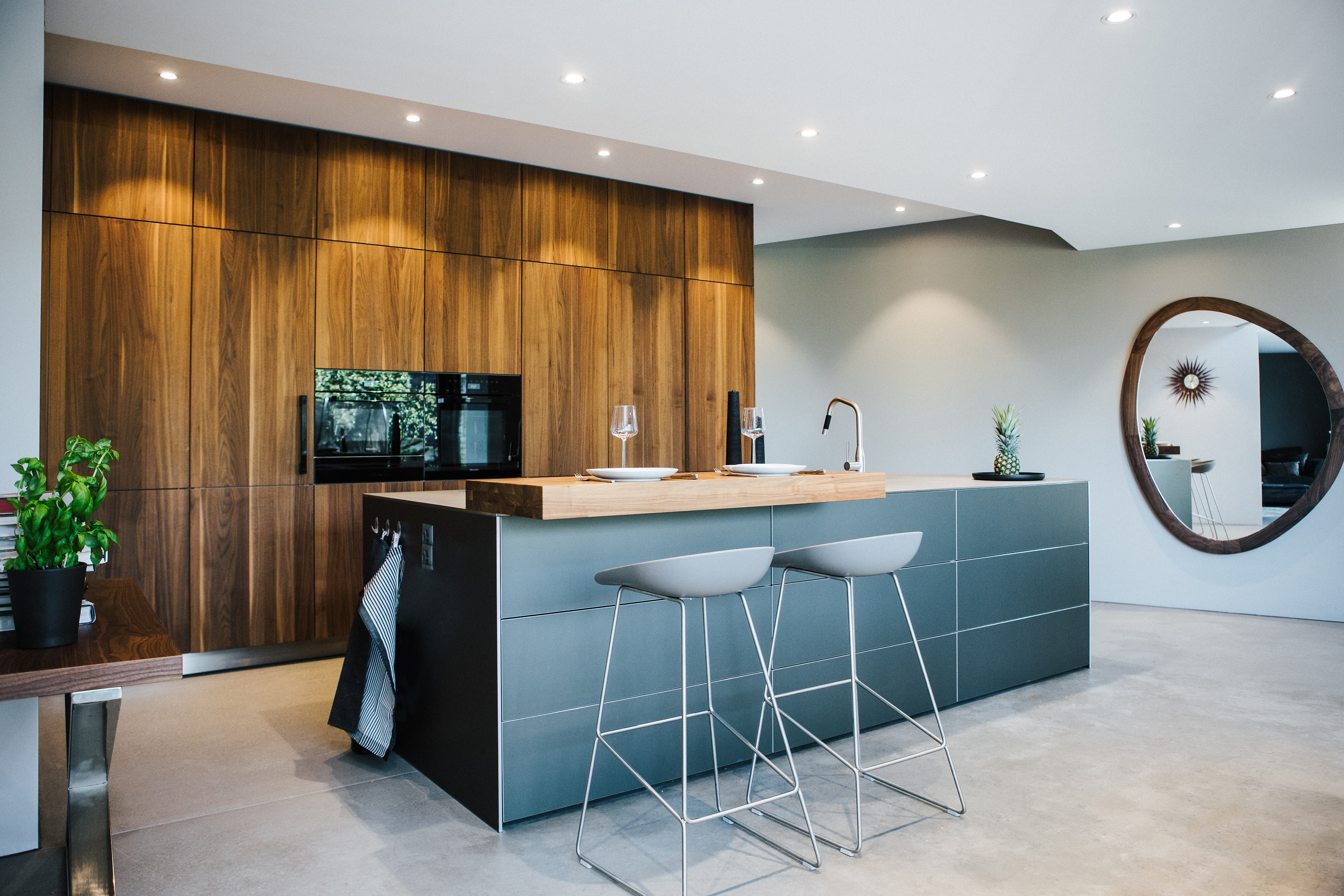 Moderne Küche mit dunkler Kochinsel, Barhockern und Wandverkleidung aus warmem Nussbaumholz.