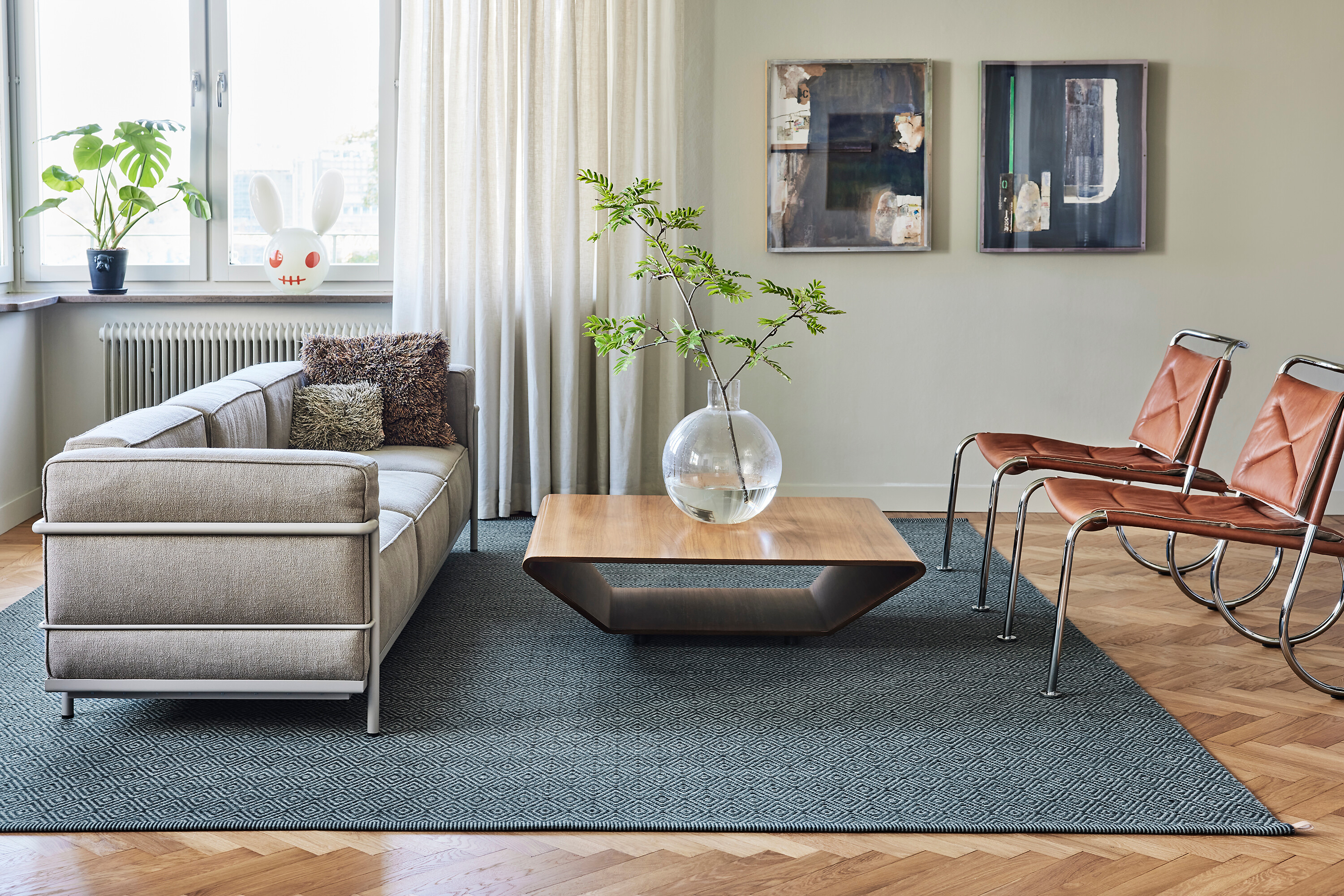 Wohnzimmer mit anthrazitfarbenem Teppich, Flachsesseln und Glastisch auf Parkett