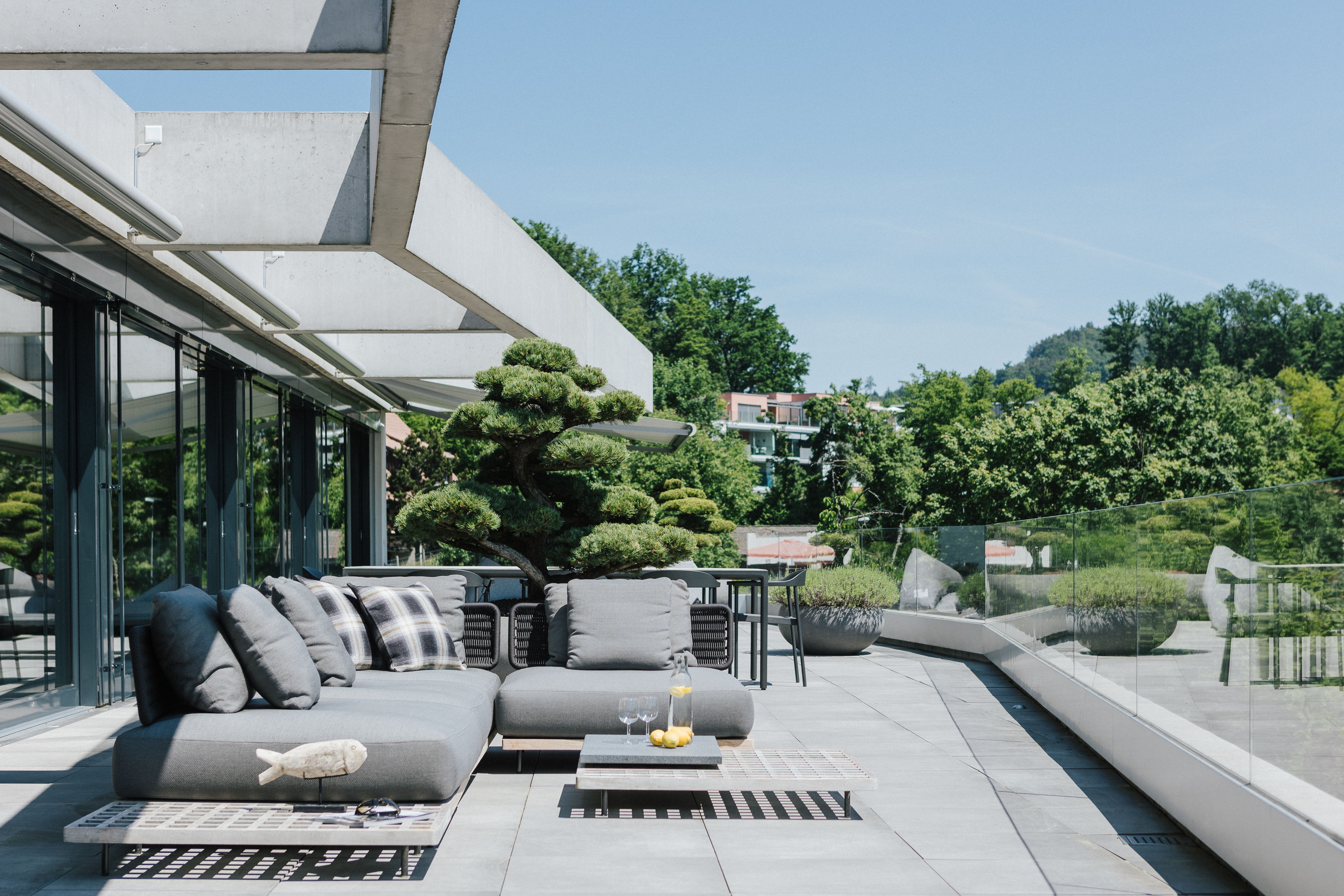 Großzügige Terrasse mit grauem Loungesofa, niedrigen Beistelltischen und Blick ins begrünte Wohnumfeld.