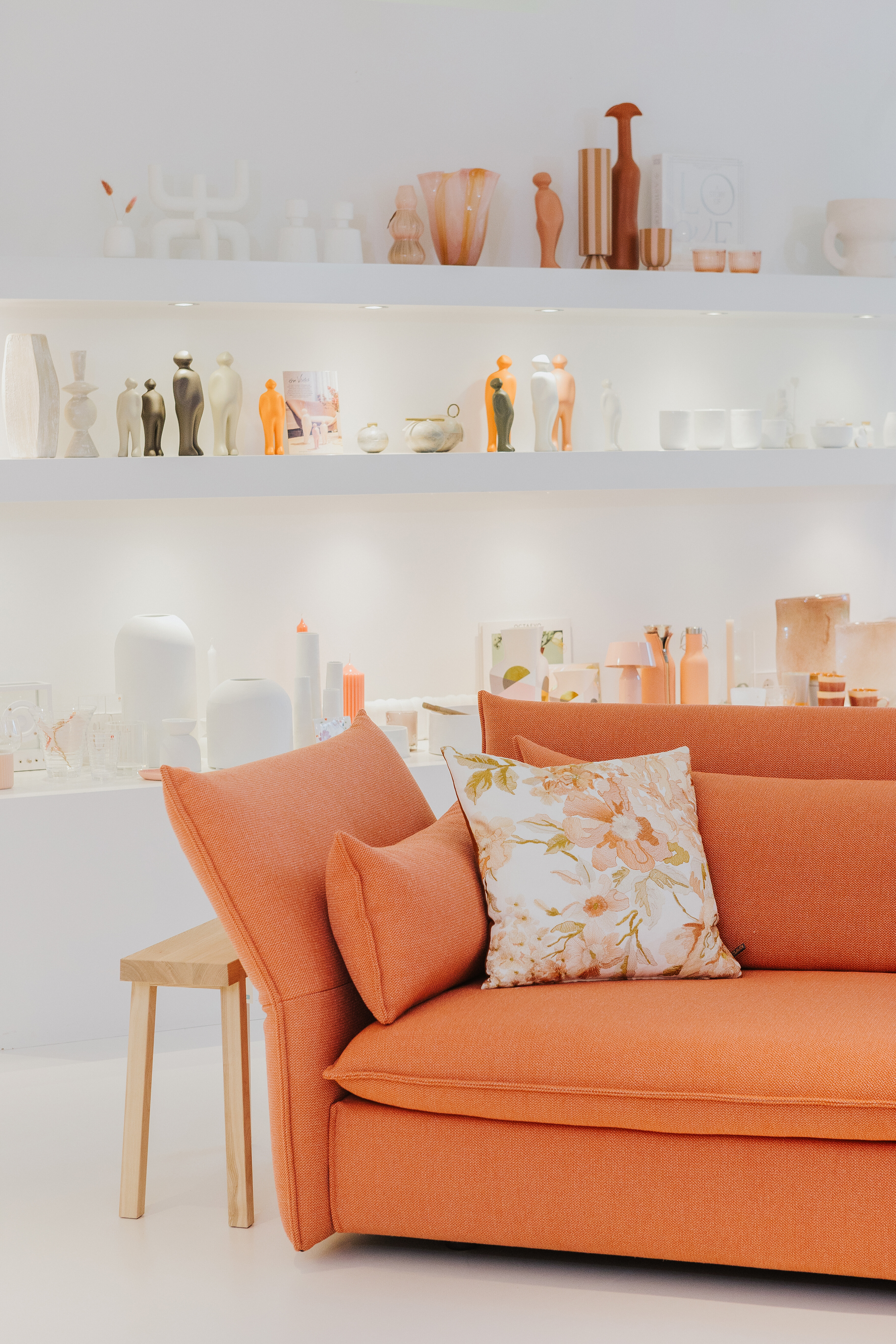 Orangefarbenes Sofa mit floralem Kissen vor Regal mit Wohnaccessoires in der Ausstellung Tiengen