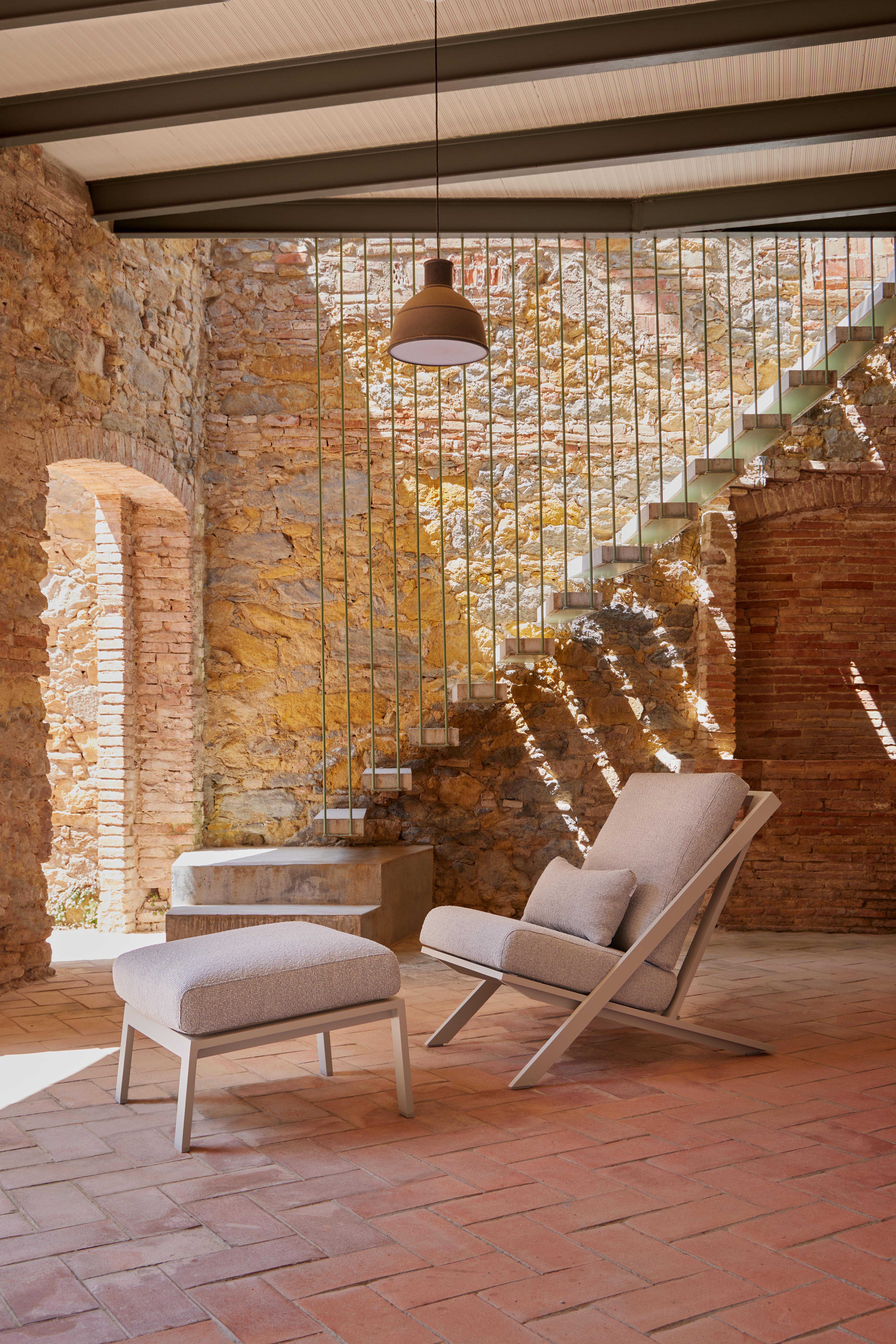 Lounge-Sessel mit Hocker in gemauertem Innenhof vor Treppe mit Metallgeländer