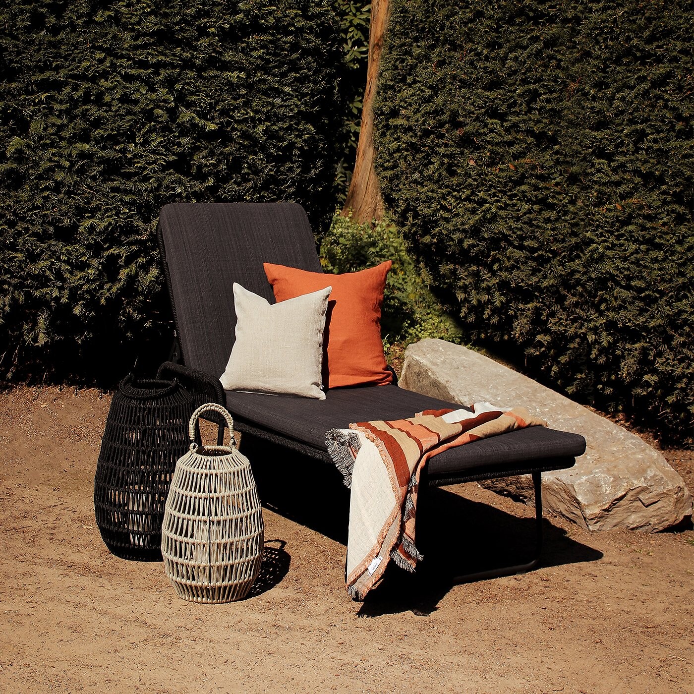 Schwarze Gartenliege von Lambert mit Kissen, Plaid und Körben im Sonnenlicht