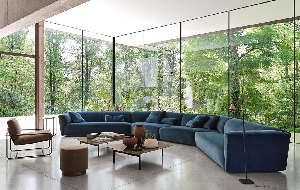 langes geschwungenes Sofa in Blau in verglastem Wohnbereich mit Blick ins umgebende Grün