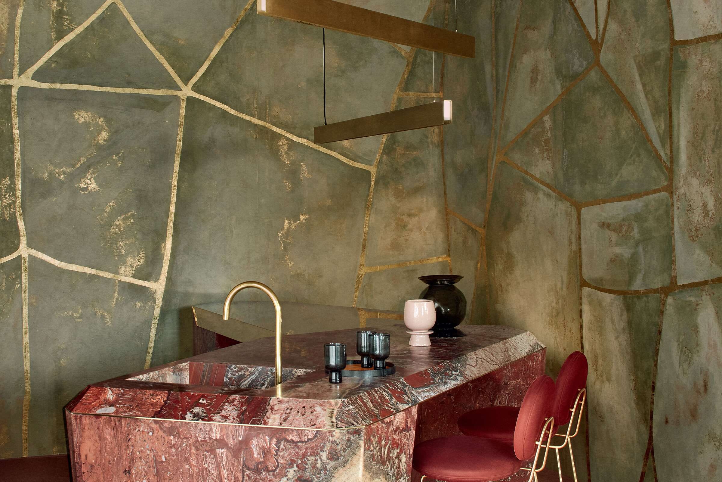 Barbereich mit grünlich strukturierter Wand, rötlicher Marmorplatte und modernen Hängeleuchten