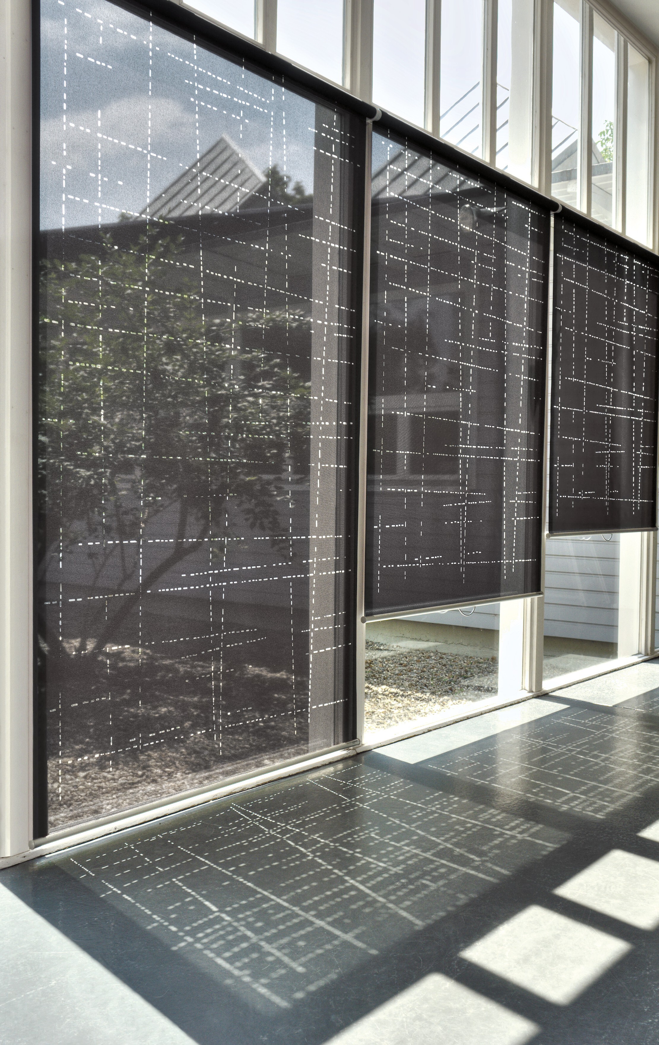 Halbtransparente Rollos mit grafischem Muster an hoher Fensterfront im Tageslicht