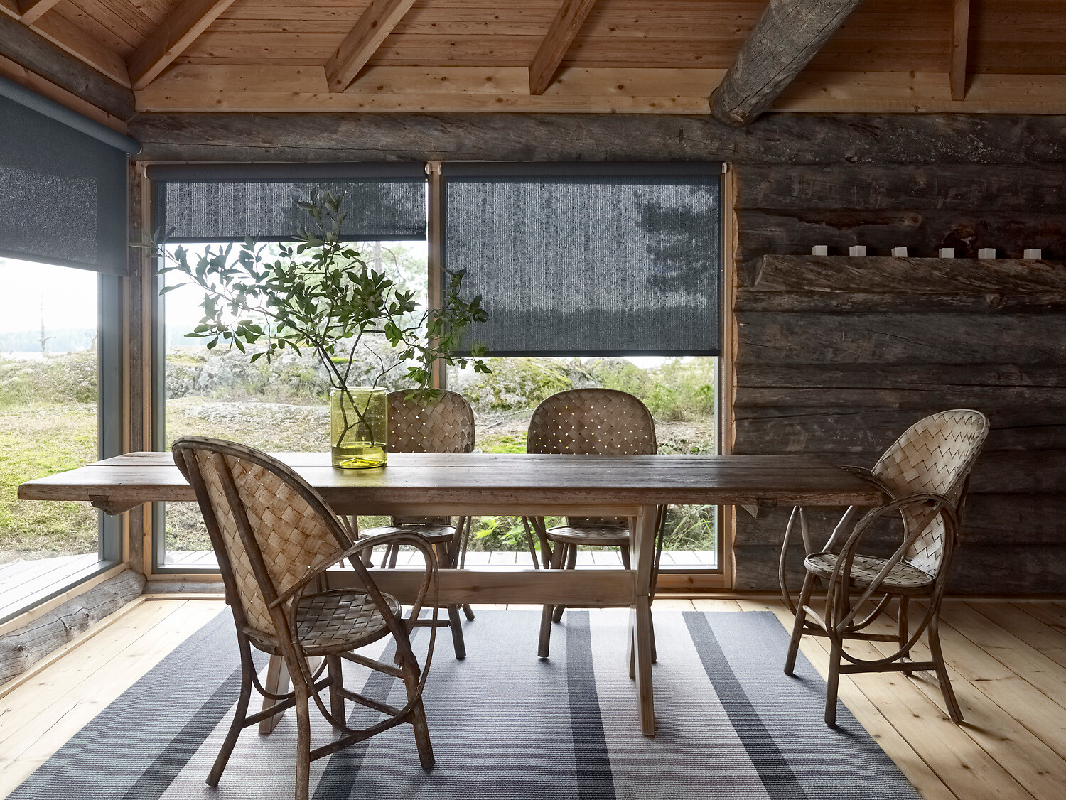 Rustikaler Essplatz mit Holzstühlen auf gestreiftem Teppich, Fenster mit Rollos