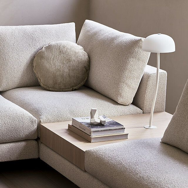 Beiges Sofa mit kleiner Leuchte und Buch auf Ablagefläche