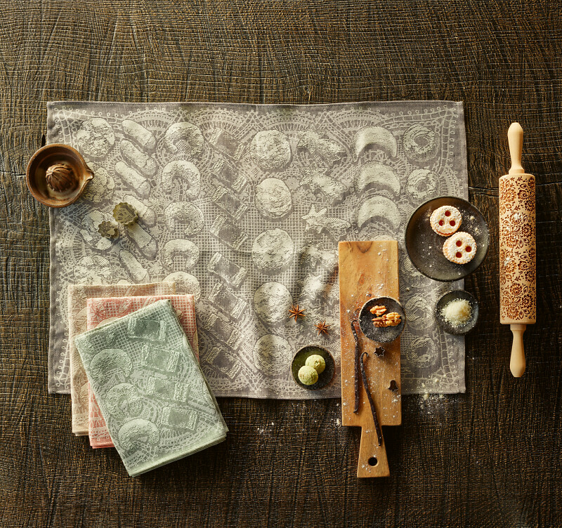 Küchentextilien auf dunklem Stoff mit Gebäck, Teigrolle und Holzbrett