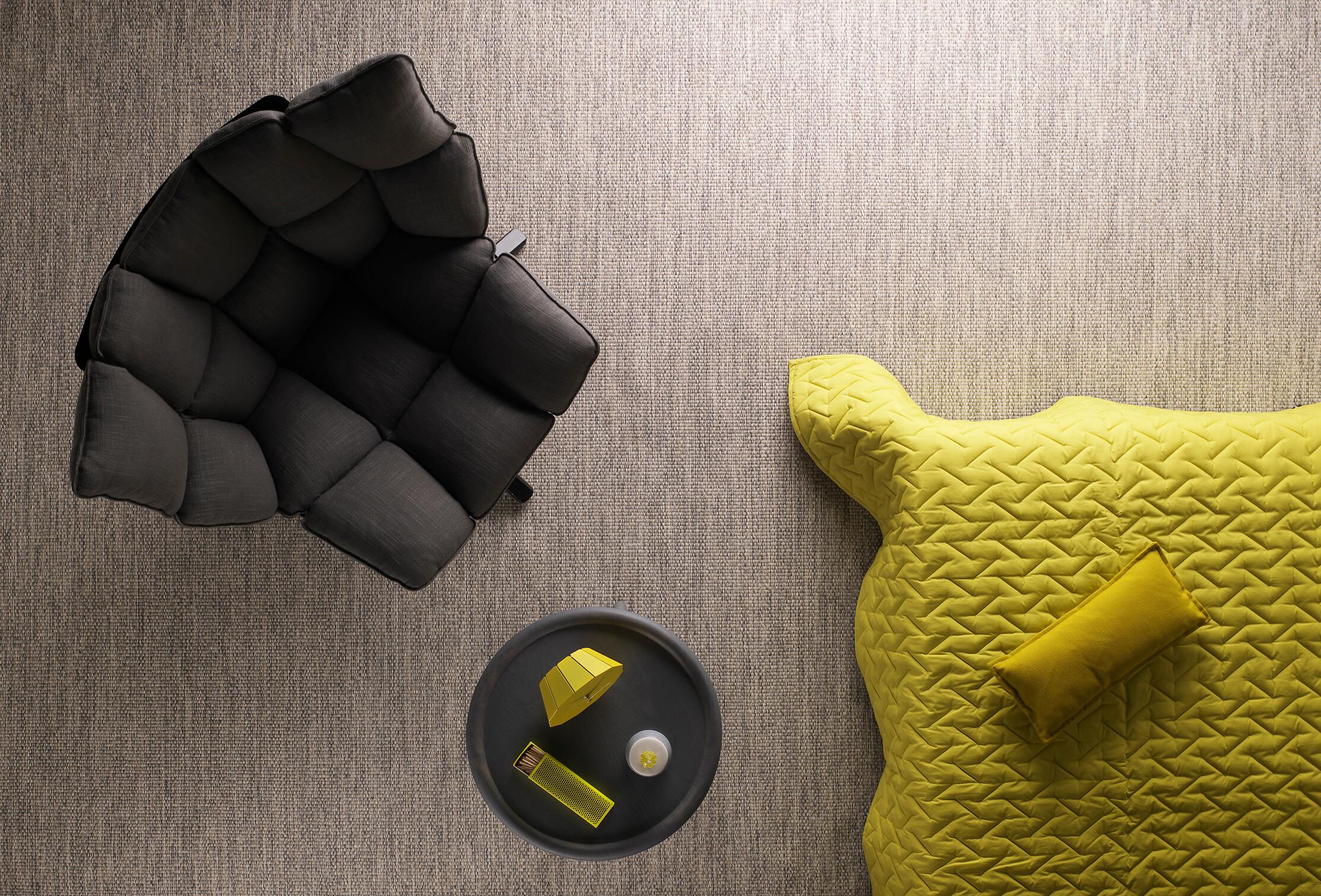 Raumansicht mit strukturierter Teppichfläche, schwarzem Sessel und gelbem Textilobjekt