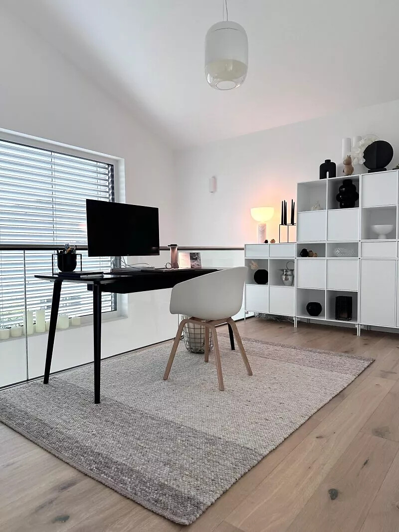 Arbeitszimmer mit Holzfußboden, hellem Teppich und minimalistischem Mobiliar