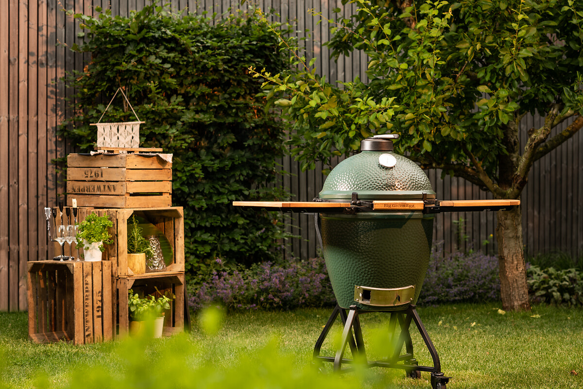 Geschlossener Big Green Egg Grill im Garten mit seitlichen Ablagen und rustikaler Deko